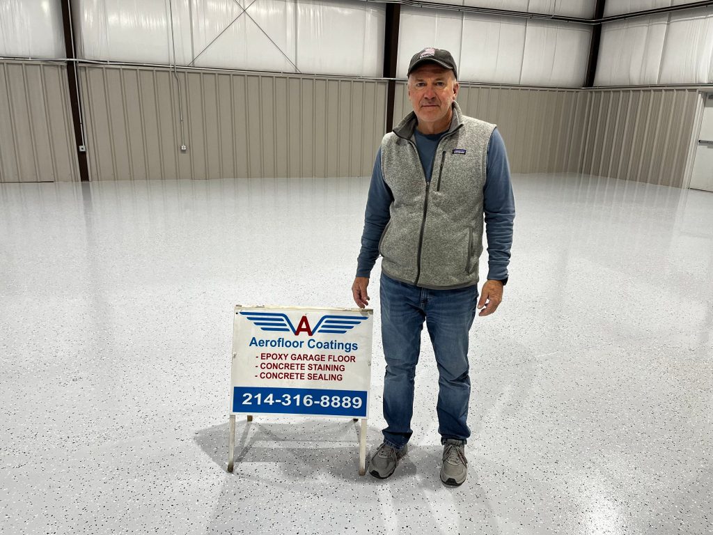 Kelly Wright, owner of Aerofloor Coating Services, poses in his hangar beside a company info sign.