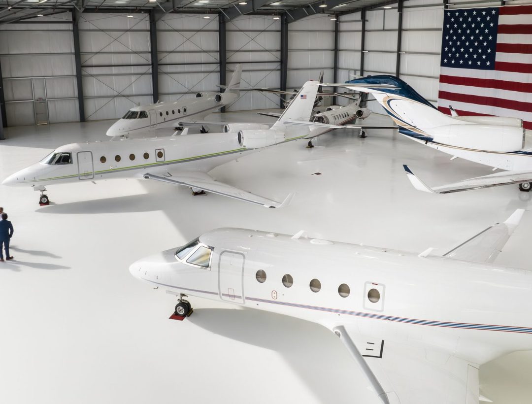 Five private planes parked inside a massive hangar bearing the United States flag.

This drone shot was taken with full permission and co-operation of the airport staff and the pilots of the aircraft.